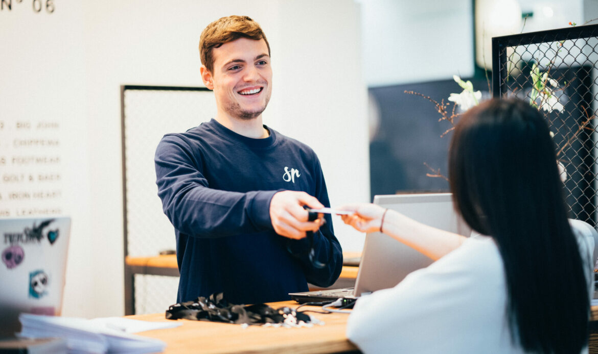 Junger Mann arbeitet an einem Check-in Schalter und hilft einer Frau