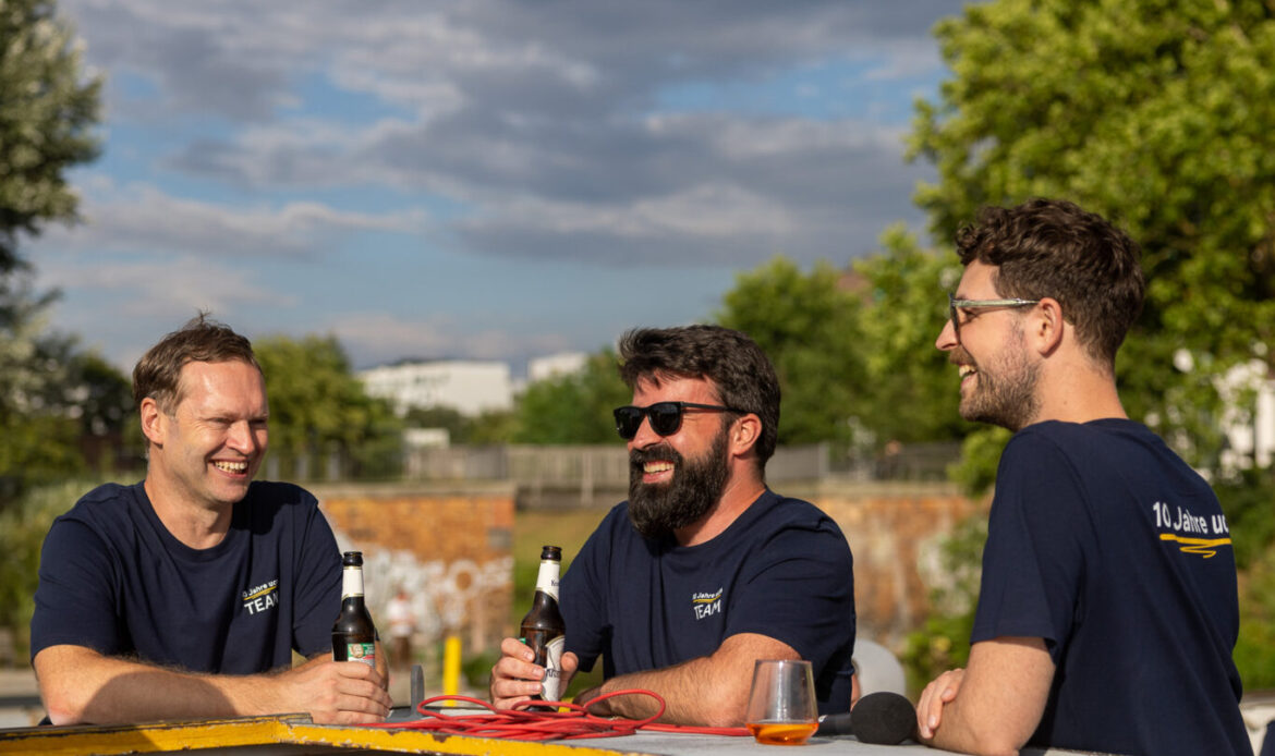 Drei Personen auf einem Boot, lachend und mit Getränk