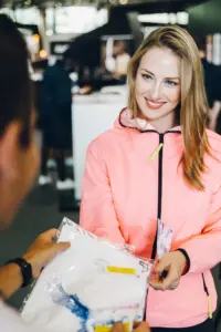 Junge Frau in rosa Jacke übergibt ein eingepacktes T-Shirt an eine andere Person