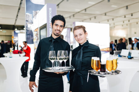 Zwei Kellner*innen mit vollen Tabletts bei der Arbeit auf einer Messe